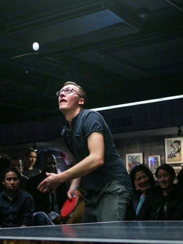 man about to paddle ping pong ball surrounded by group of people